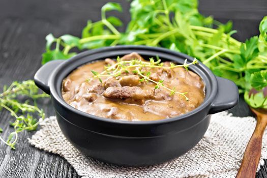 Beef goulash in tomato sauce with sprigs of thyme in a pan on burlap, spoon, parsley on dark wooden board