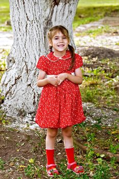 Girl in a red dress under a tree on a background of green grass