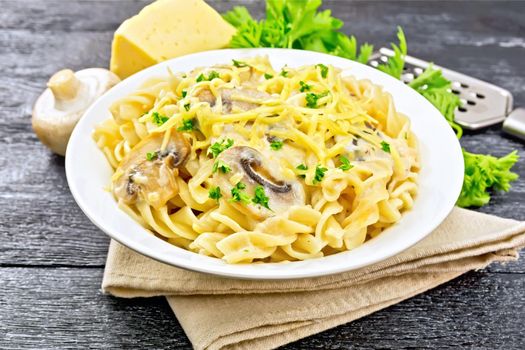 Fusilli pasta with mushrooms in creamy sauce, parsley and grated cheese in a plate on napkin on wooden board background