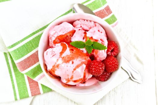 Ice cream crimson with raspberry berries, syrup and mint in white bowl, a spoon on napkin on wooden board background from above