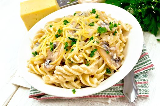 Fusilli pasta with champignons in creamy sauce, parsley and grated cheese in a dish on kitchen towel on wooden board background