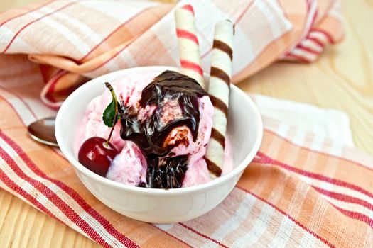 Ice cream cherry in a bowl, chocolate syrup and wafer rolls on a napkin against the background of wooden boards