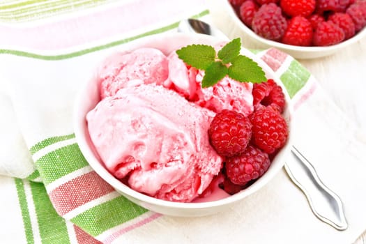 Ice cream crimson with raspberry berries and mint in white bowl, a spoon on napkin on wooden board background