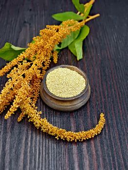 Groats amaranth in a clay bowl, brown flower with green leaves on a background of wooden boards