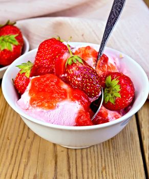 Strawberry ice cream in a white bowl with strawberries and spoon, napkin on a wooden boards background