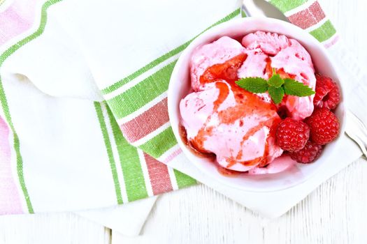 Ice cream crimson with raspberry berries, syrup and mint in white bowl, a spoon on towel on the background of wooden board from above