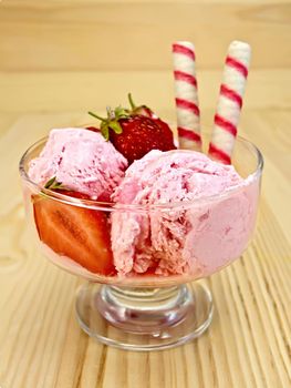 Strawberry ice cream in a glass bowl with wafer rolls and strawberries on a wooden boards background