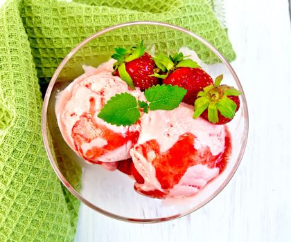 Strawberry ice cream in a glass with strawberries, mint and strawberry syrup, napkin on the background light wooden boards on top
