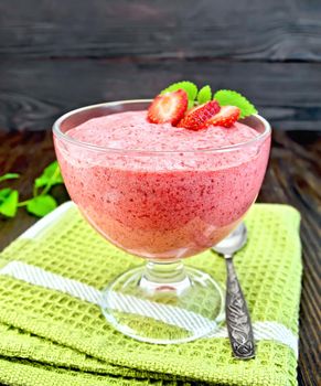 Jelly air strawberry in a glass bowl, a spoon on a green towel, mint on the background of wooden boards