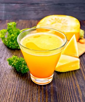 Pumpkin juice in a tall glass with pieces of pumpkin, parsley on a wooden boards background