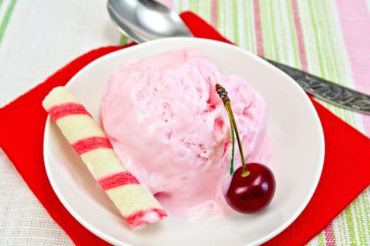 Cherry ice cream in a bowl with wafer rolls on a red paper napkin, spoon on a background of striped linen tablecloths