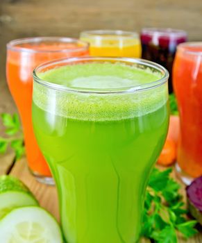 Five tall glassfuls with juice of carrot, cucumber, beetroot, tomato and pumpkin, vegetables, parsley on a wooden boards background