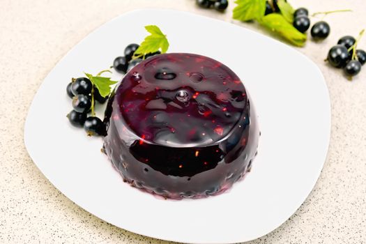 Jelly from a black currant with berries in a plate on a napkin on the background of a granite table