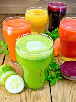 Five tall glasses with the juice of carrot, cucumber, beetroot, tomato and pumpkin with vegetables and parsley on a wooden boards background
