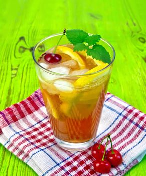 Lemonade in a glass with a cherry, lemon and orange, mint on a napkin on a green wooden board