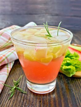 Lemonade with rhubarb and rosemary in a glass, the stems and leaves of rhubarb, a doily on a wooden boards background
