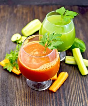 The juice of carrot and cucumber in two wineglass, vegetables and parsley on a wooden board background