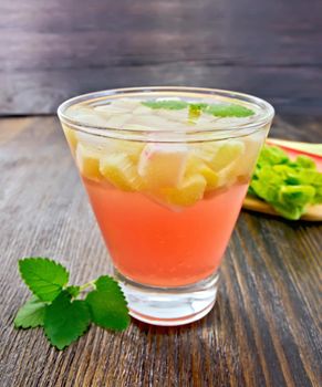 Lemonade with rhubarb and mint in a glass, the stems and leaves of rhubarb on a dark wooden board