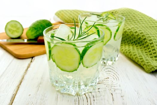 Lemonade with a cucumber and rosemary in two glassful, a knife, a cucumber and a napkin on a wooden boards background