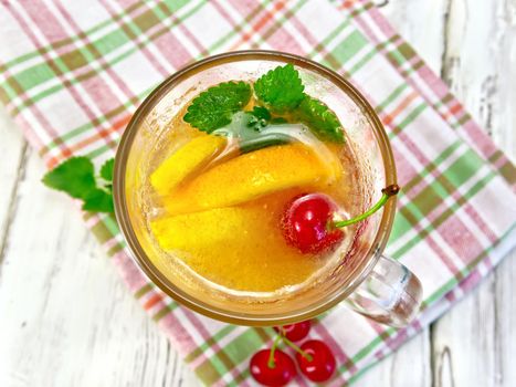 Lemonade in a wineglass with a cherry, lemon and orange, mint on a napkin on the background of wooden boards on top