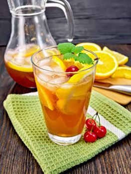 Lemonade in a glassful and jug with a cherry, lemon, orange and mint on a green towel, a board with fruits on a wooden board background