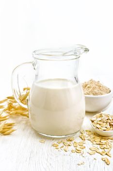 Oat milk in a jug, flour in bowl, oatmeal in spoon, stalks oaten on white board background
