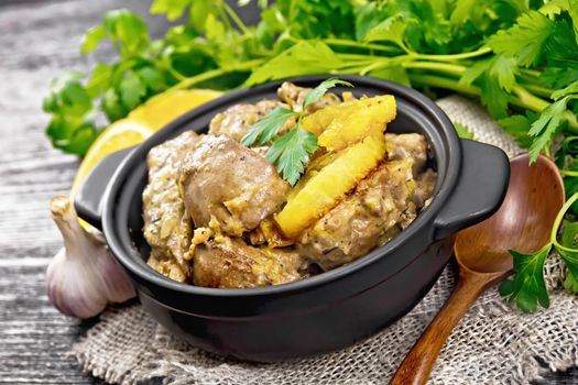 Chicken liver stewed with oranges, sour cream, soy sauce and Provence herbs in a small pan on burlap, a spoon and parsley on black wooden board background