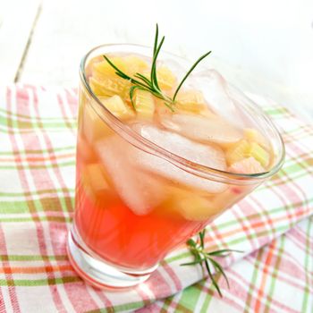 Lemonade with rhubarb and rosemary in a glass on a napkin on a wooden boards background