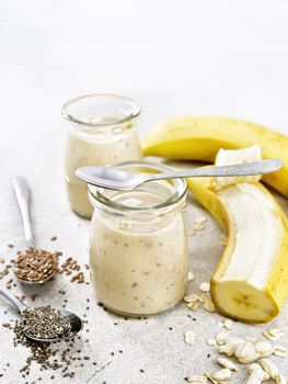 Milkshake with chia seeds, flax seeds, oatmeal, puffed rice and banana in two glass jars on a brown granite table background