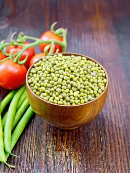 Green lentils mung in a bowl, pods of beans and red tomatoes on a wooden board background