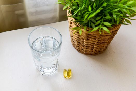 Omega-3, spirulina, chlorophyll capsules and glass of water on white wooden table. Dietary supplements, biologically active additives. vitamin pills. Health support.