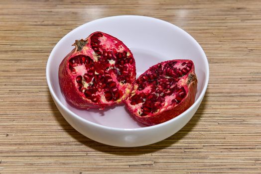 Halved red ripe pomegranate fruits in a white bowl. Natural pomegranate closeup.