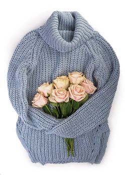 White winter sweater with a bouquet delicate roses. Spring and winter mood composition. Flat lay, top, top view.