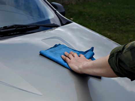 Man wipes car bonnet with rag.