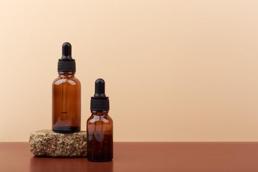 Skin serums in glass dark brown bottles with natural stone on brown table against beige background with copy space. Concept of skin care and beauty treatment