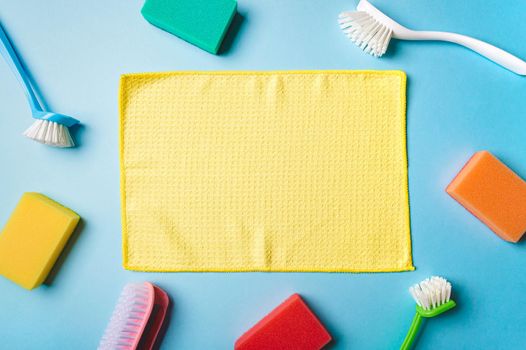 House cleaning product and empty yellow napkin in center, blue background, copy space. Flat lay or top view. Cleaning service or housekeeping concept with space for text or design in center
