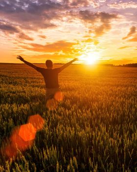 Silhouette of a man raise his hands up to sunset or sunrise on the field with young rye or wheat in the summer with a cloudy sky background. 