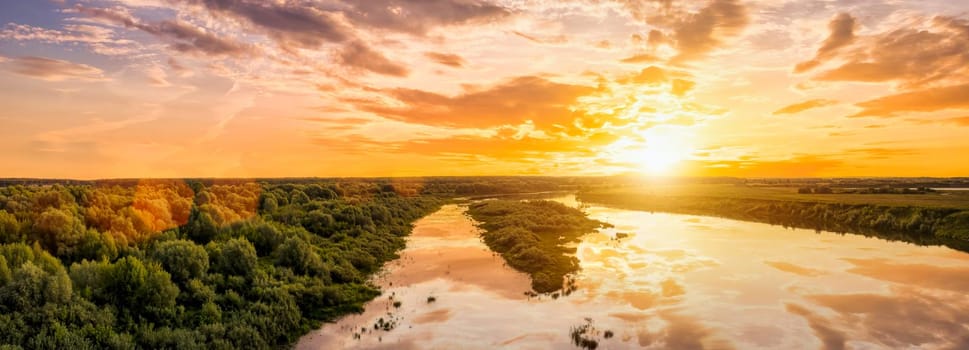 Aerial view to sunset on the river at summer evening with clouds and willow trees. Water reflection of a sky.