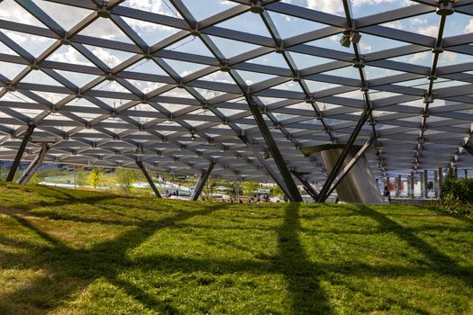 Glass roof with oval metal partitions. Shadow from the base on the grass.