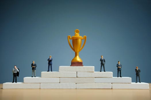 Business strategy conceptual photo - Miniature of businessman stands on podium ladder with golden trophy. Image photo