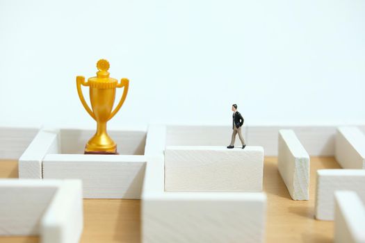 Business strategy conceptual photo - Miniature of businessman on a labyrinth maze seeking the golden trophy. Image photo