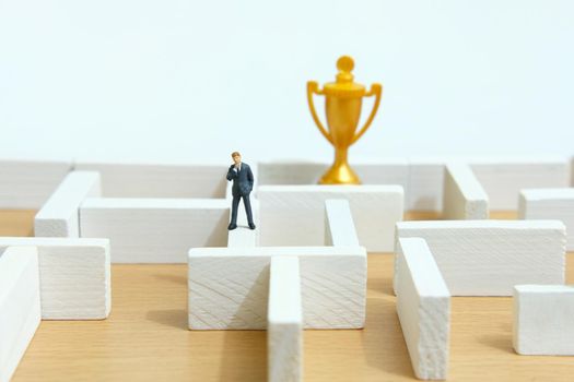 Business strategy conceptual photo - Miniature of businessman on a labyrinth maze seeking the golden trophy. Image photo