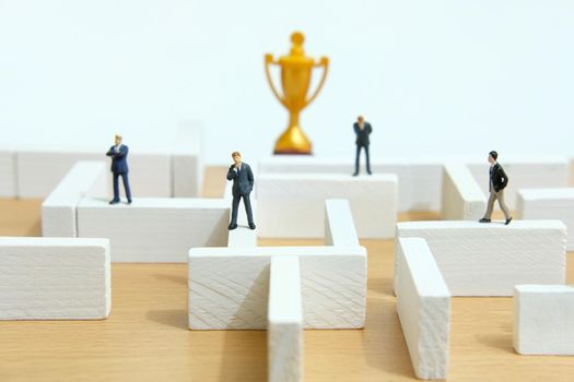 Business strategy conceptual photo - Miniature of businessman on a labyrinth maze seeking the golden trophy. Image photo