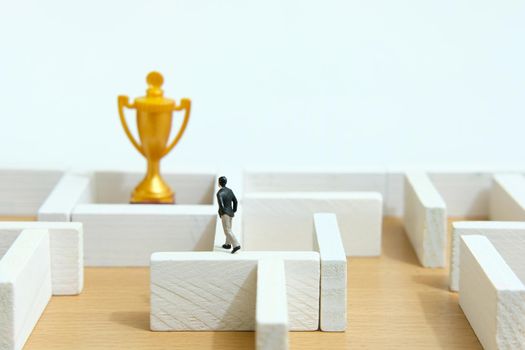 Business strategy conceptual photo - Miniature of businessman on a labyrinth maze seeking the golden trophy. Image photo