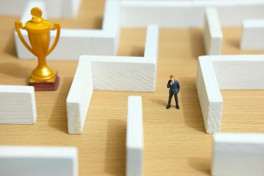 Business strategy conceptual photo - Miniature of businessman on a labyrinth maze seeking the golden trophy. Image photo