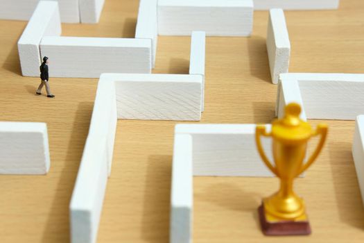 Business strategy conceptual photo - Miniature of businessman on a labyrinth maze seeking the golden trophy. Image photo