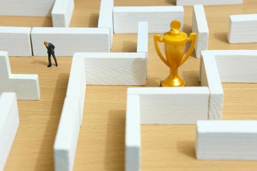 Business strategy conceptual photo - Miniature of businessman on a labyrinth maze seeking the golden trophy. Image photo