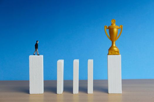 Miniature business concept - businessman walking in stairway obstacle wall to reach golden trophy. Image photo