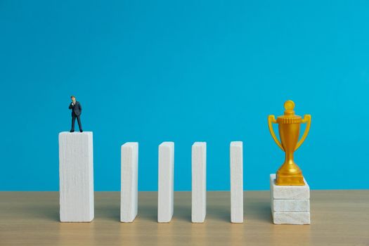 Miniature business concept - businessman thinking in front of obstacle wall to reach golden trophy. Image photo