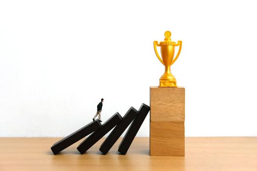 Miniature business concept - businessman walking on collapse stairway to reach golden trophy. Image photo